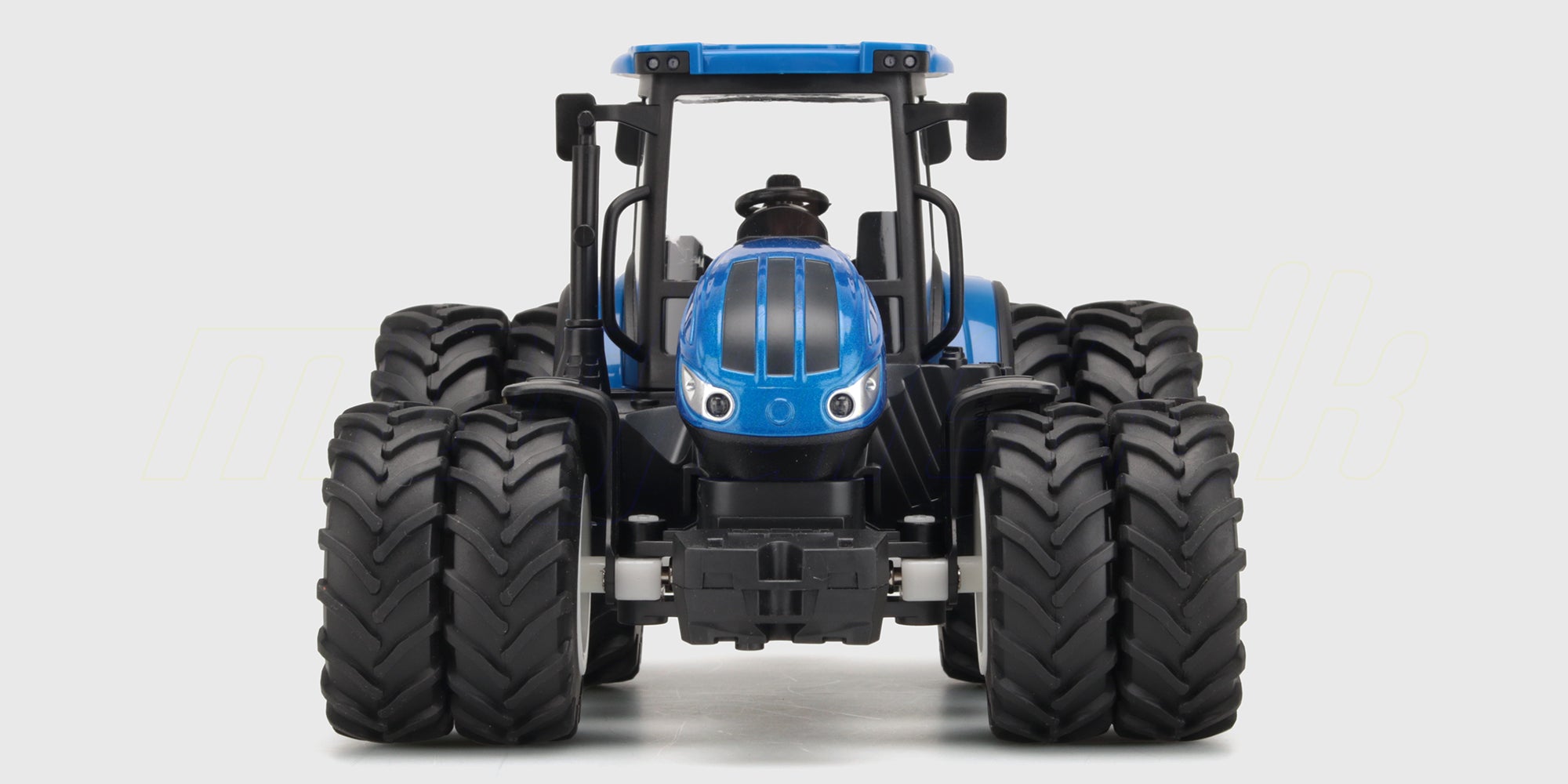 Grøn fjernstyret traktor med gul frontlæsser og fjernbetjening vist på hvid baggrund.