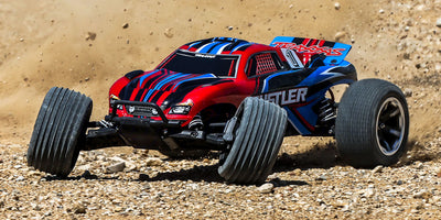 Blå Traxxas Rustler 2WD fjernstyret stadiontruck med grove offroad-dæk set forfra på hvid baggrund.