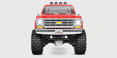 Rød Traxxas TRX-4M Chevrolet K10 crawler, der forcerer store sten i ujævnt terræn.
