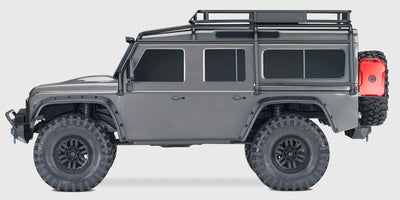 Grå Traxxas TRX-4 Land Rover Defender crawler kører gennem mudret terræn i naturen.